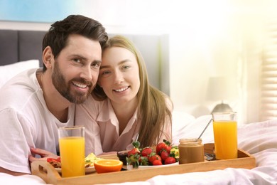 Image of Happy couple having breakfast in bed on sunny morning. Space for text