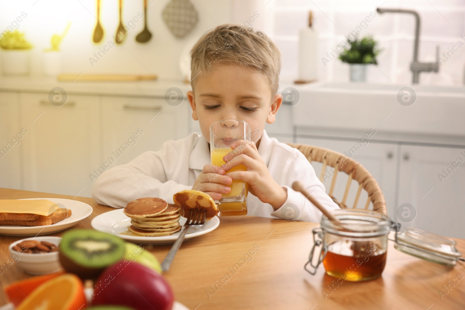 Image of Little boy having breakfast at table on kitchen on sunny morning