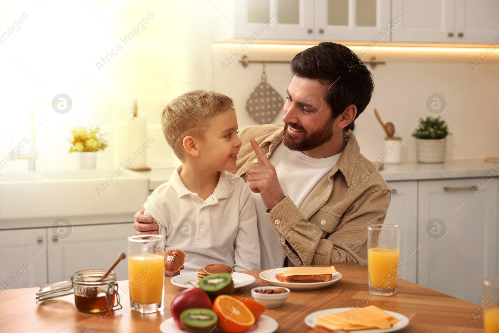 Image of Father and his cute little son having breakfast at table in kitchen on sunny morning