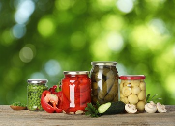 Image of Jars with pickled vegetables and mushrooms on wooden table outdoors, space for text