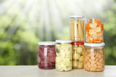 Image of Jars with pickled vegetables and mushrooms on white wooden table outdoors, space for text