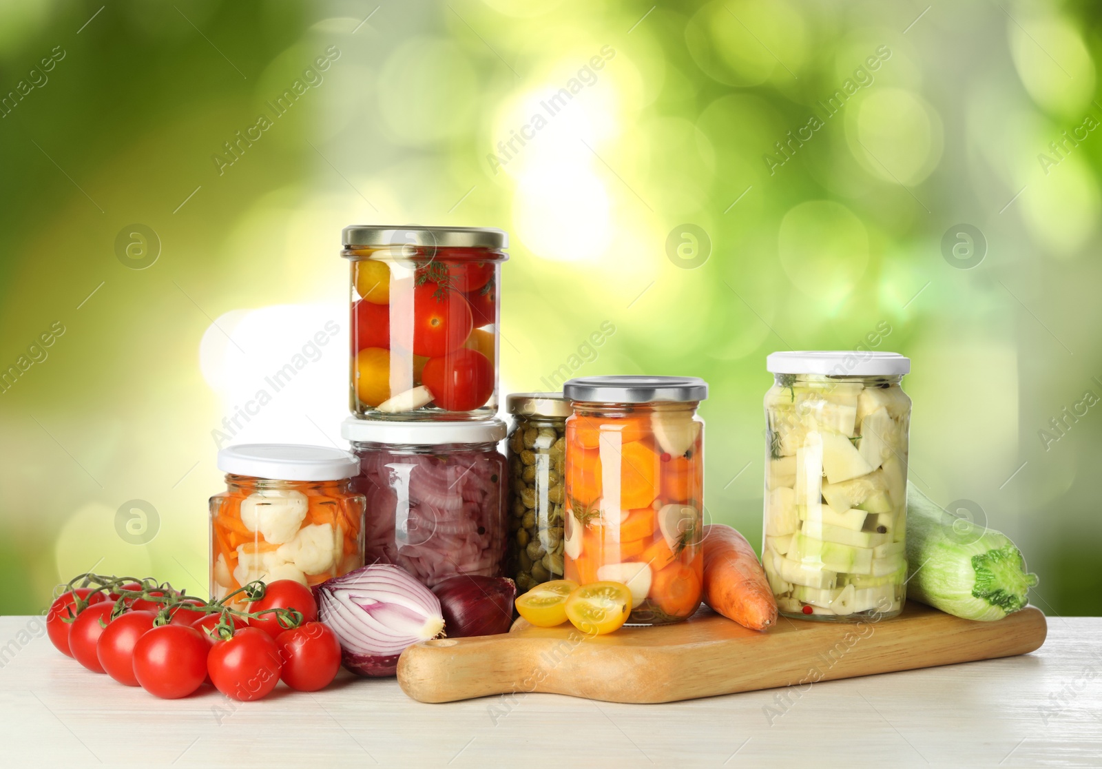 Image of Jars with pickled vegetables on white wooden table outdoors