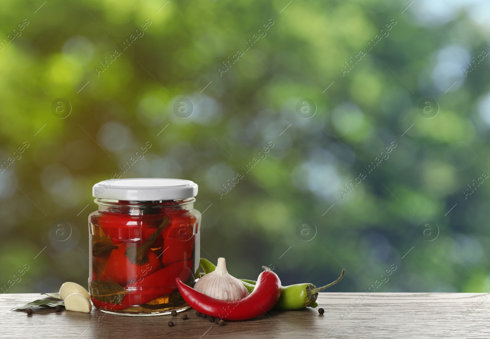 Image of Jar with pickled peppers on wooden table outdoors, space for text