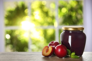 Image of Jar with preserved plums on wooden table indoors, space for text