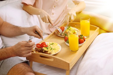 Couple eating tasty breakfast in bed on sunny morning, closeup