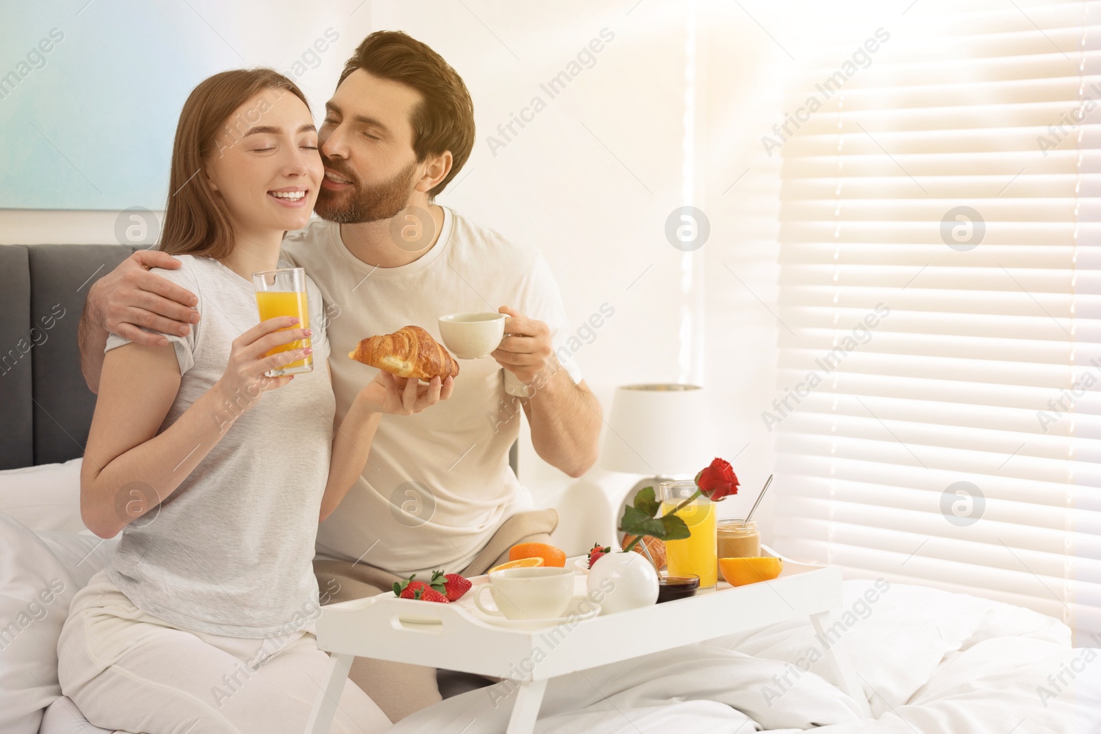 Image of Lovely couple having breakfast in bedroom on sunny morning. Space for text