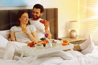 Happy couple eating tasty breakfast in bed at home on sunny morning