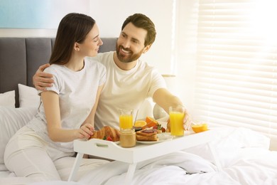 Happy couple having breakfast in bedroom on sunny morning. Space for text