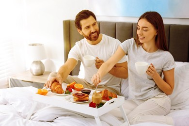 Image of Happy couple having breakfast in bedroom on sunny morning. Space for text