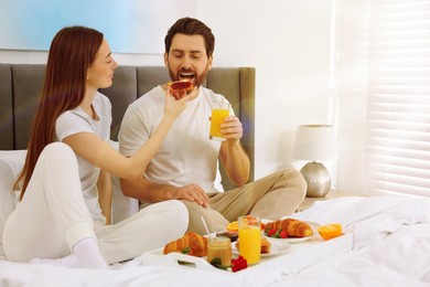 Image of Happy couple having breakfast in bedroom on sunny morning. Space for text