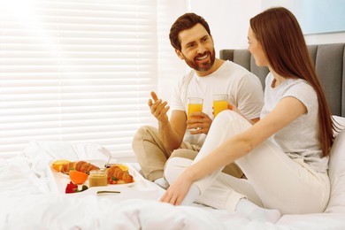 Happy couple having breakfast in bedroom on sunny morning. Space for text