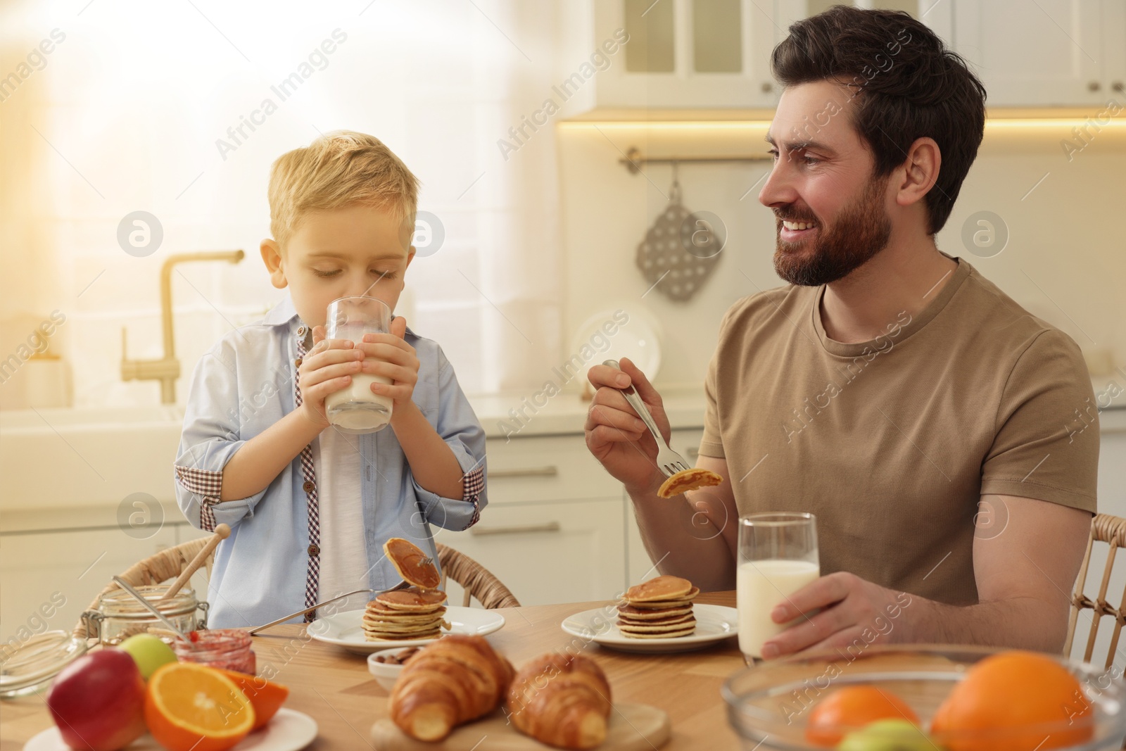 Image of Father and his cute little son having breakfast at table in kitchen on sunny morning