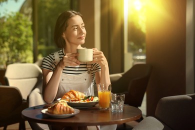 Image of Happy woman having tasty breakfast in cafe on sunny morning