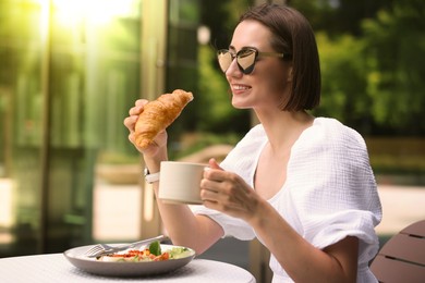 Happy woman having tasty breakfast at outdoor cafe on sunny morning