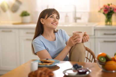 Image of Smiling woman having breakfast in kitchen on sunny morning