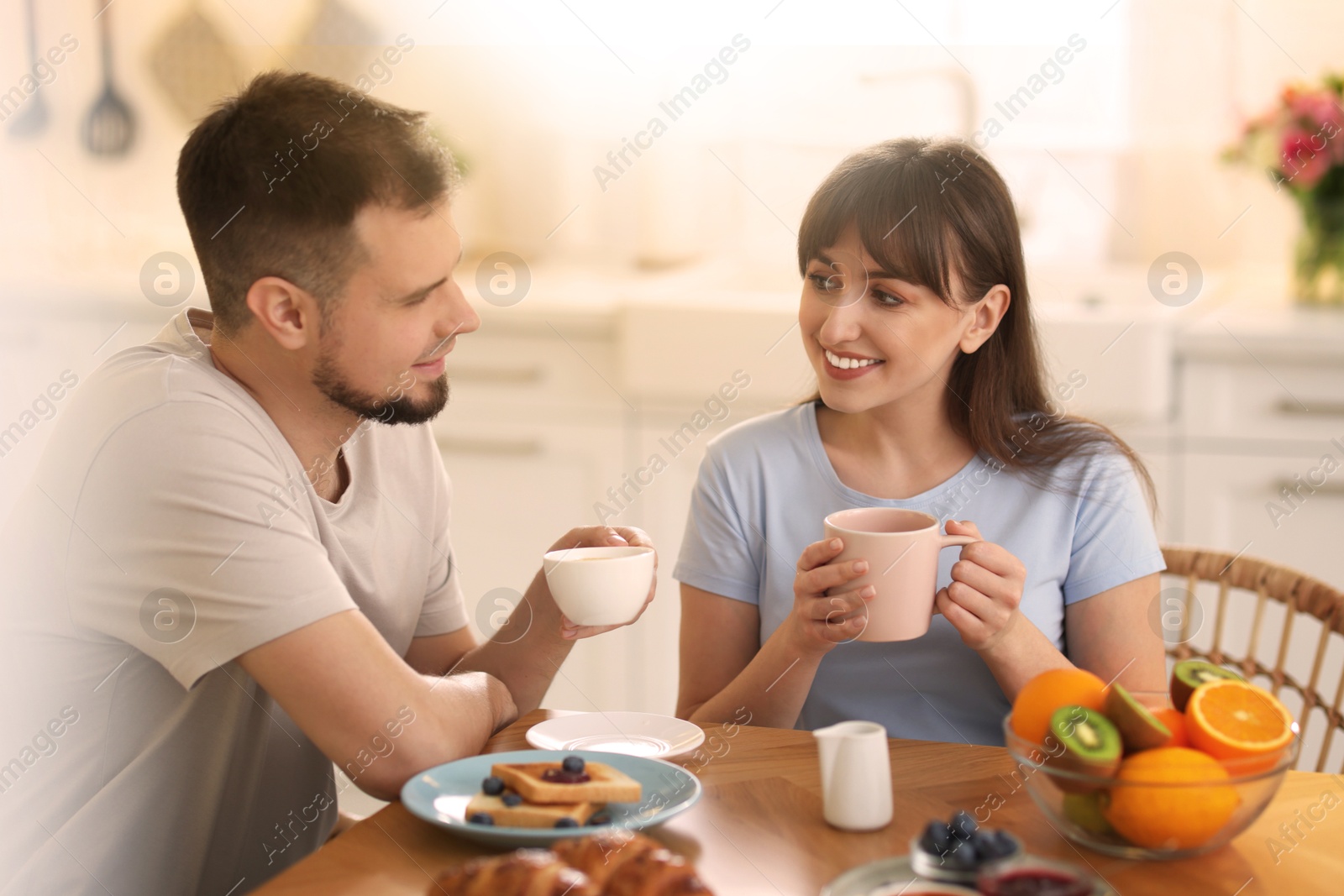 Image of Happy couple having breakfast in kitchen on sunny morning