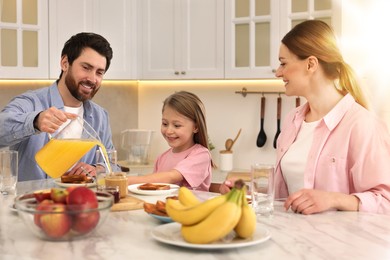 Happy family having breakfast at table in kitchen on sunny morning