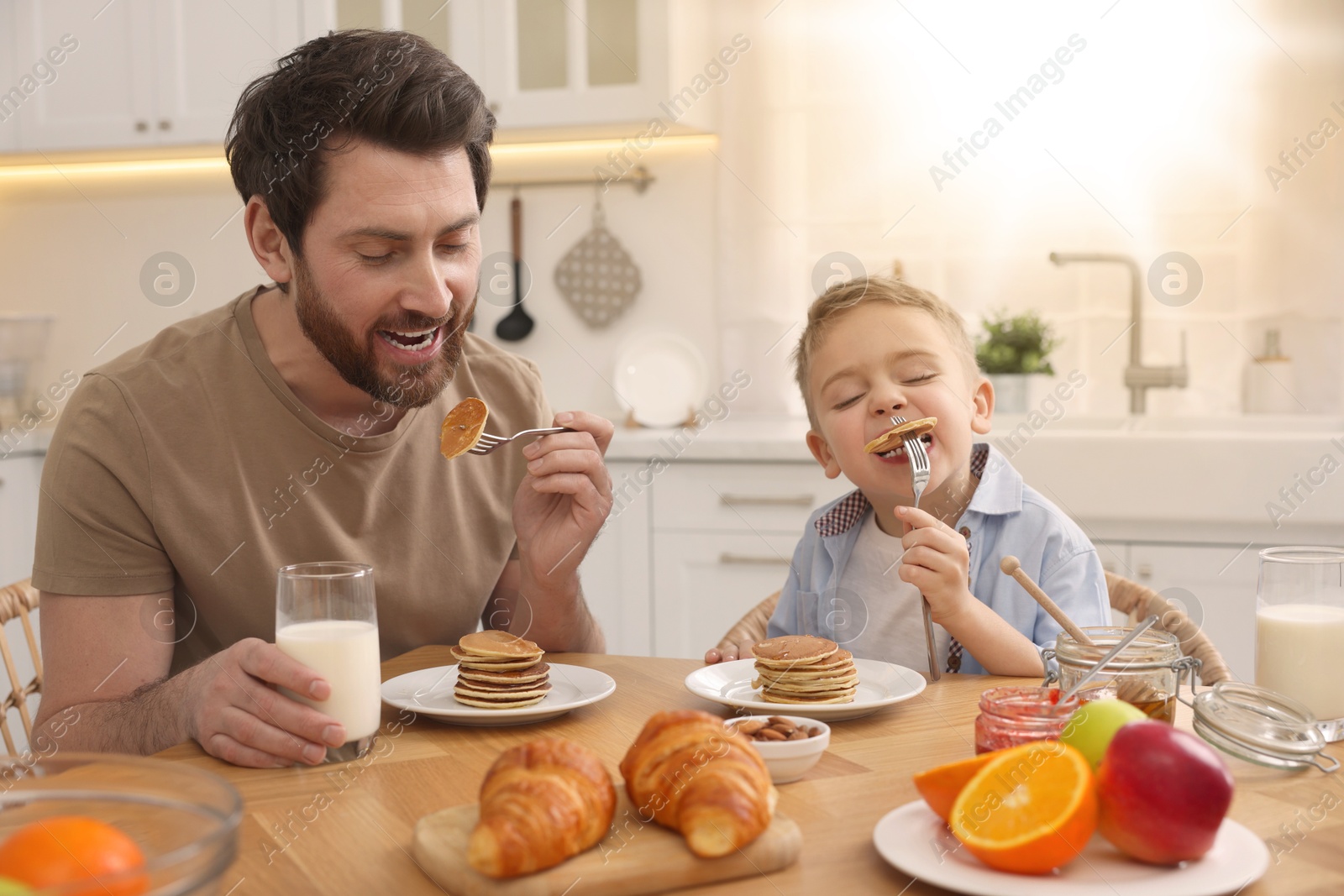 Image of Father and his cute little son having breakfast at table in kitchen on sunny morning