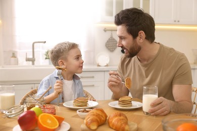 Image of Father and his cute little son having breakfast at table in kitchen on sunny morning