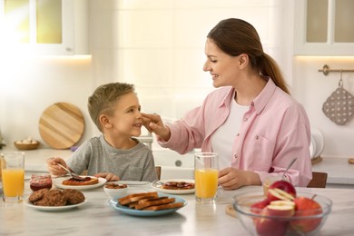 Image of Mother and her cute little son having breakfast at table in kitchen on sunny morning