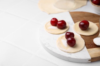 Photo of Process of making dumplings (varenyky) with cherries. Raw dough and ingredients on white table, closeup. Space for text