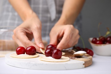 Photo of Woman making dumplings (varenyky) with cherries at white table, closeup