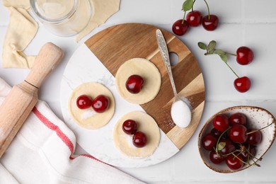 Process of making dumplings (varenyky) with cherries. Raw dough and ingredients on white tiled table, flat lay