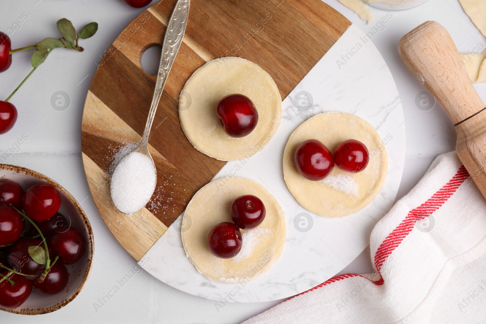 Photo of Process of making dumplings (varenyky) with cherries. Raw dough and ingredients on white tiled table, flat lay