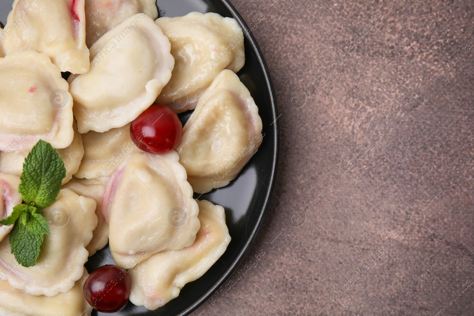 Photo of Traditional Ukrainian dumplings (varenyky) with cherries on brown table, top view. Space for text