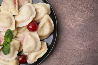 Traditional Ukrainian dumplings (varenyky) with cherries on brown table, top view. Space for text