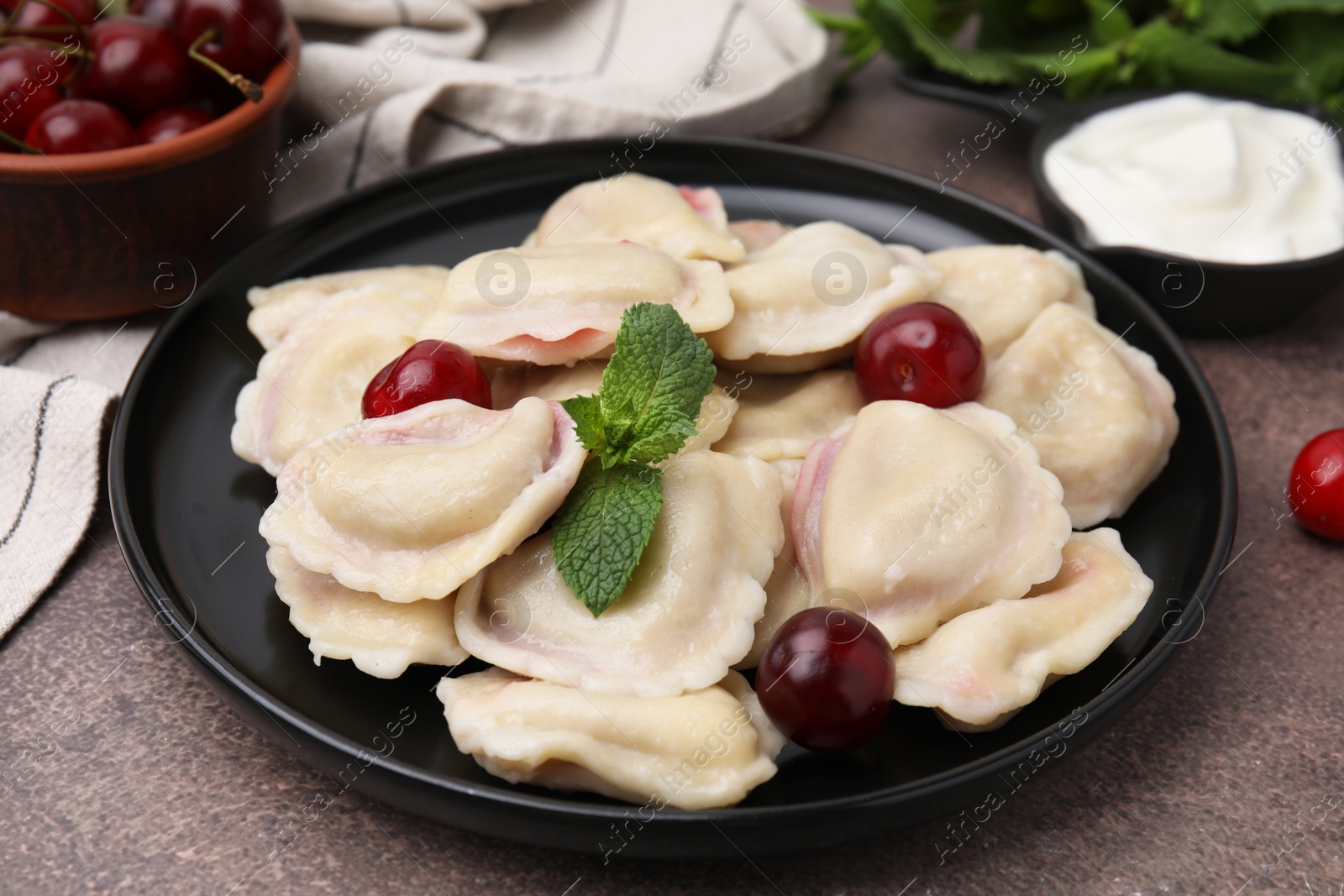 Photo of Traditional Ukrainian dumplings (varenyky) with cherries served on brown table, closeup