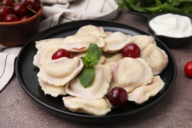 Traditional Ukrainian dumplings (varenyky) with cherries served on brown table, closeup