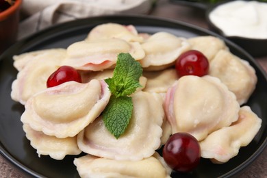 Photo of Traditional Ukrainian dumplings (varenyky) with cherries on brown table, closeup