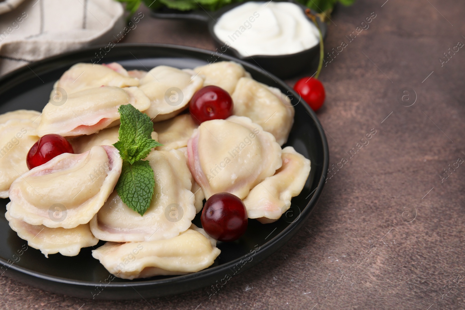 Photo of Traditional Ukrainian dumplings (varenyky) with cherries served on brown table, closeup