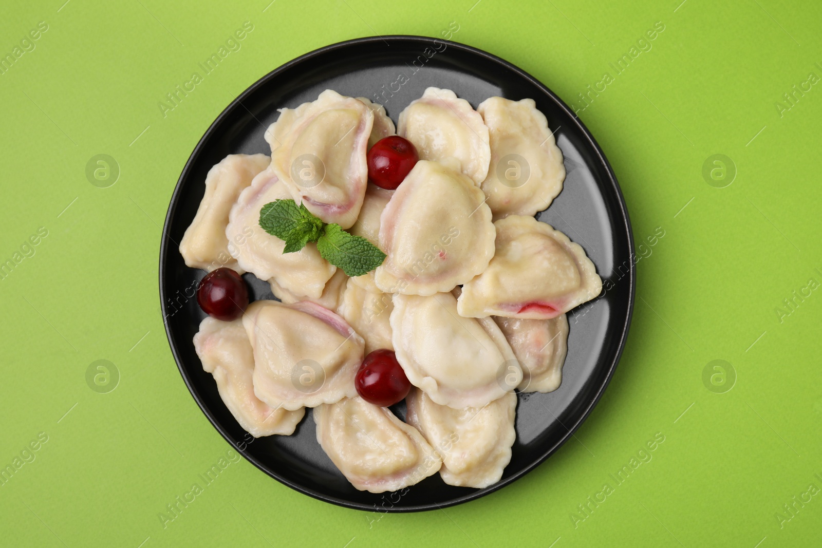 Photo of Traditional Ukrainian dumplings (varenyky) with cherries on green background, top view