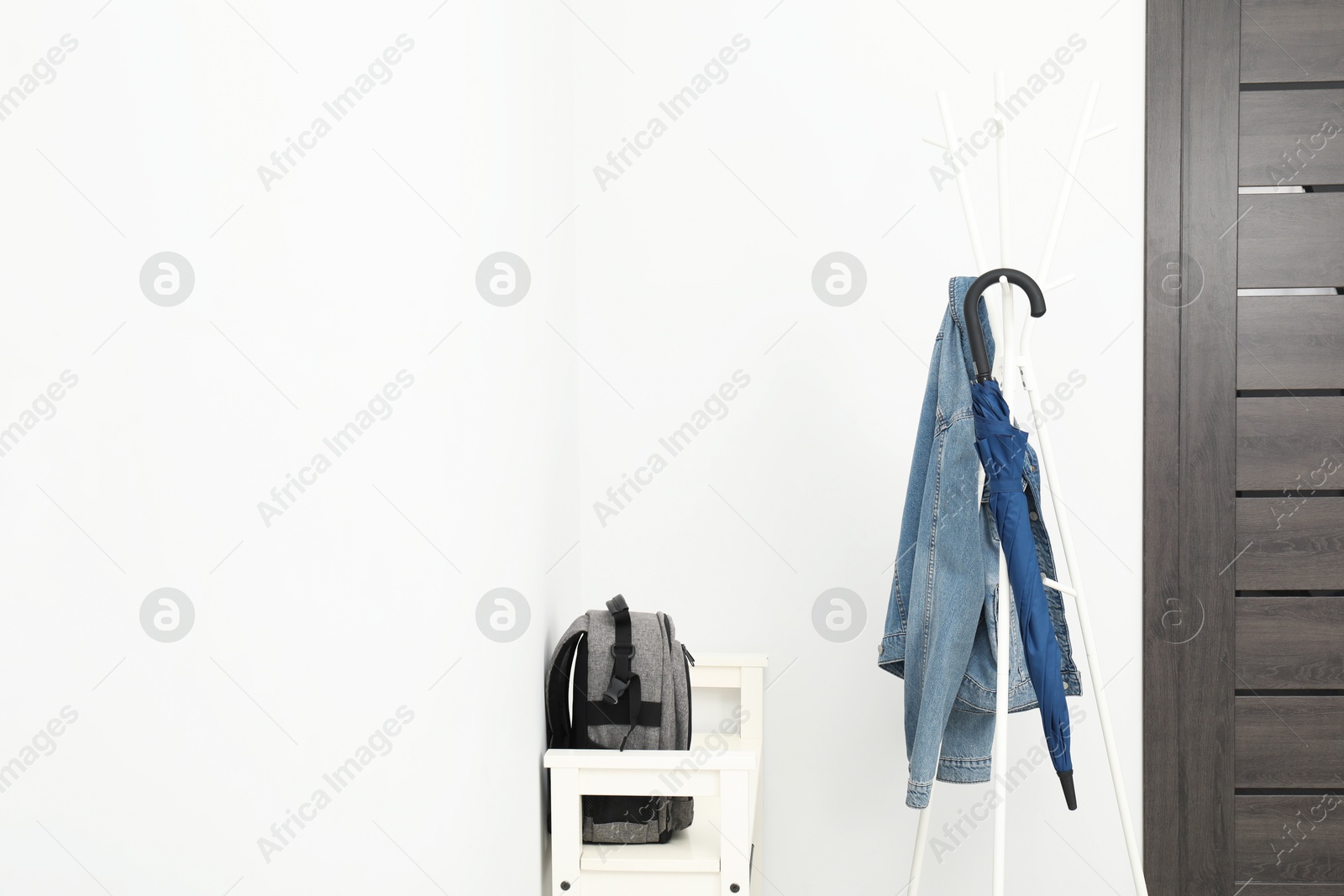 Photo of Blue umbrella and denim jacket on clothing rack near shoe storage bench with backpack in hallway, space for text