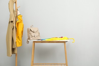 Colorful umbrellas and backpack on storage bench near rack with coats against light grey background