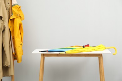 Photo of Colorful umbrellas on white table and rack with coats against light grey background