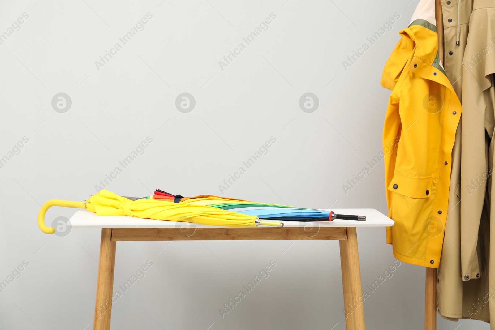 Photo of Colorful umbrellas on white table and rack with coats against light grey background