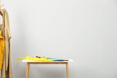 Colorful umbrellas on white table and rack with coats against light grey background, space for text