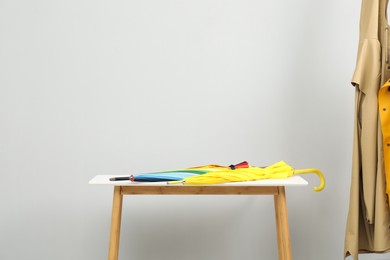 Colorful umbrellas on white table and coats against light grey background