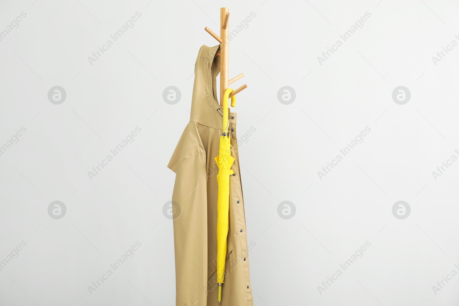 Photo of Yellow umbrella and raincoat on clothing rack against light grey background