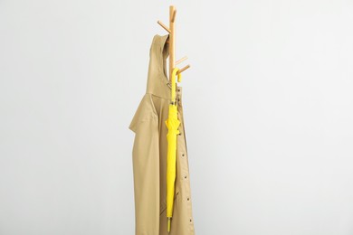 Photo of Yellow umbrella and raincoat on clothing rack against light grey background