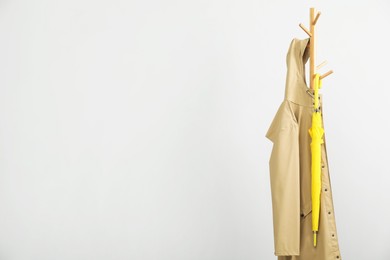 Photo of Yellow umbrella and raincoat on clothing rack against light grey background, space for text