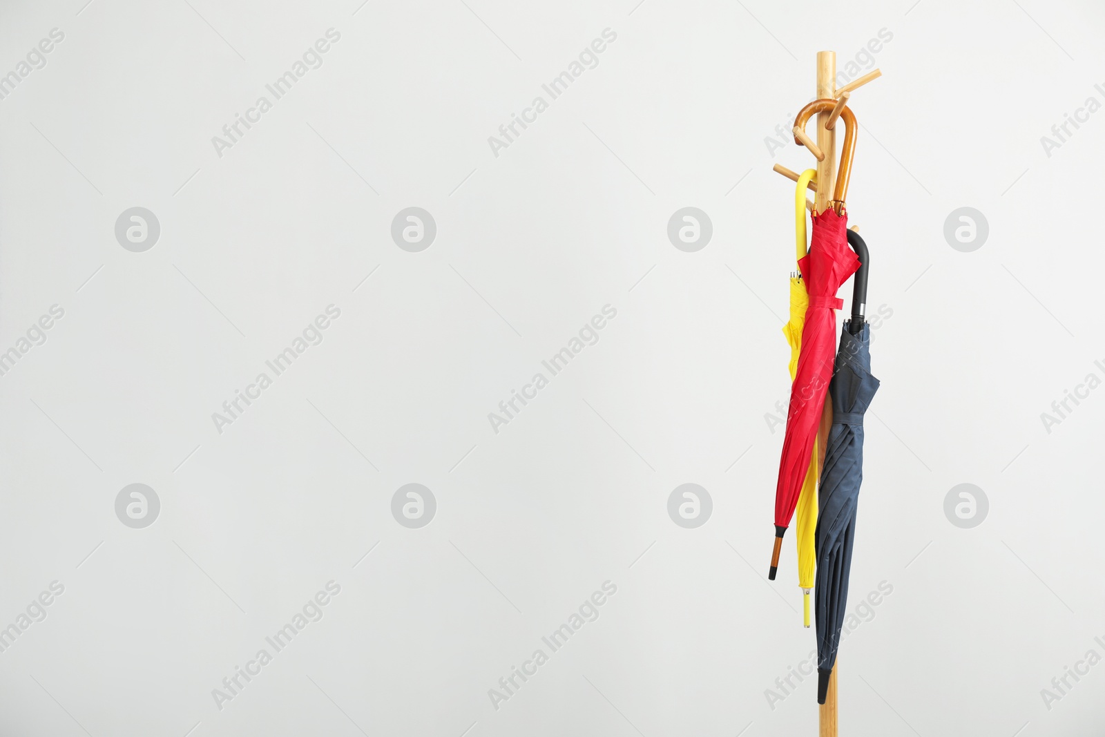 Photo of Colorful umbrellas on clothing rack against light grey background, space for text