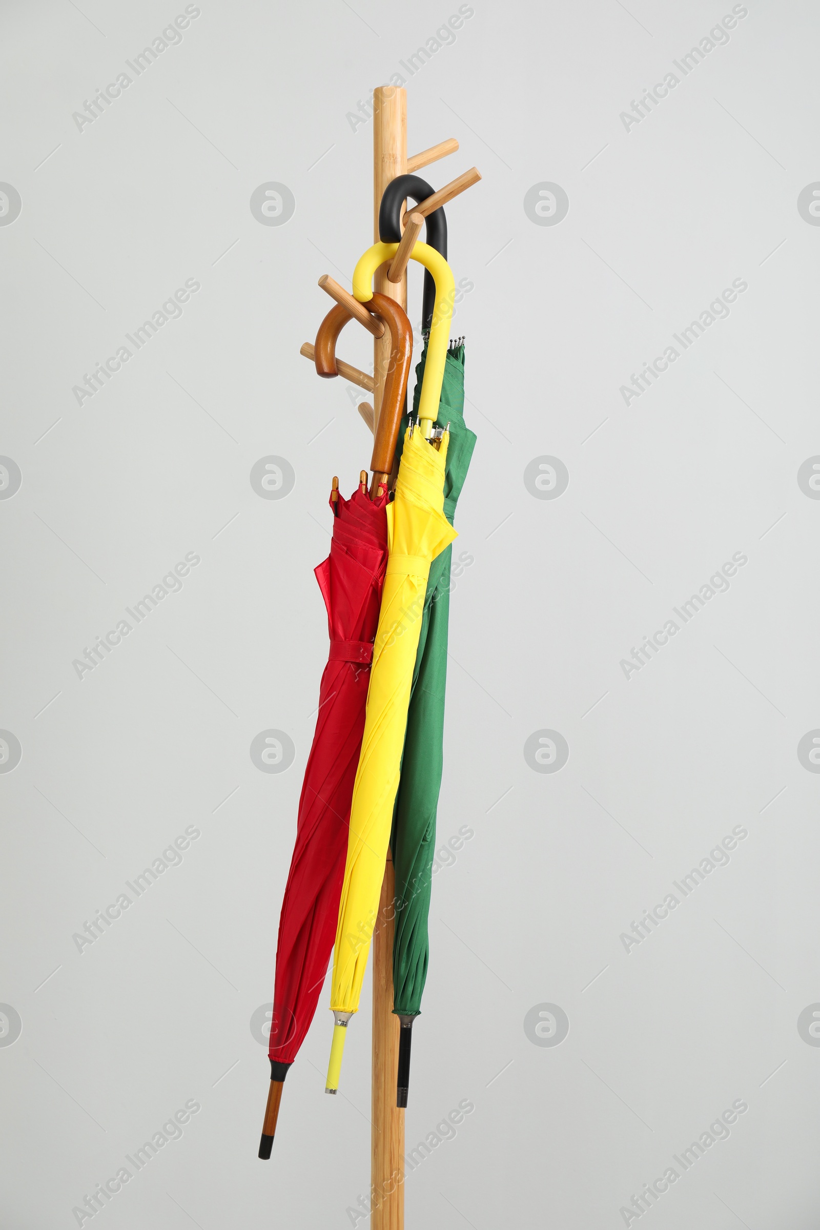 Photo of Colorful umbrellas on clothing rack against light grey background