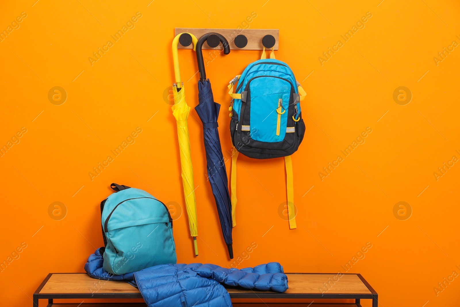 Photo of Colorful umbrellas, backpacks and jacket on wooden bench near orange wall