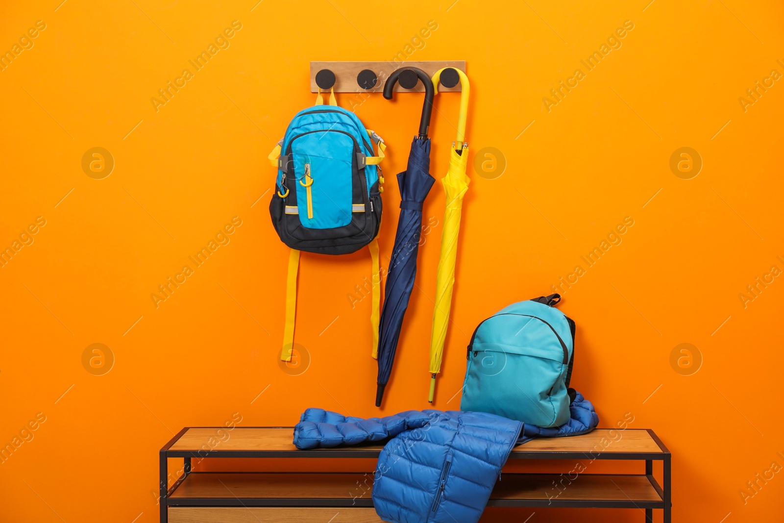 Photo of Colorful umbrellas, backpacks and jacket on wooden bench near orange wall