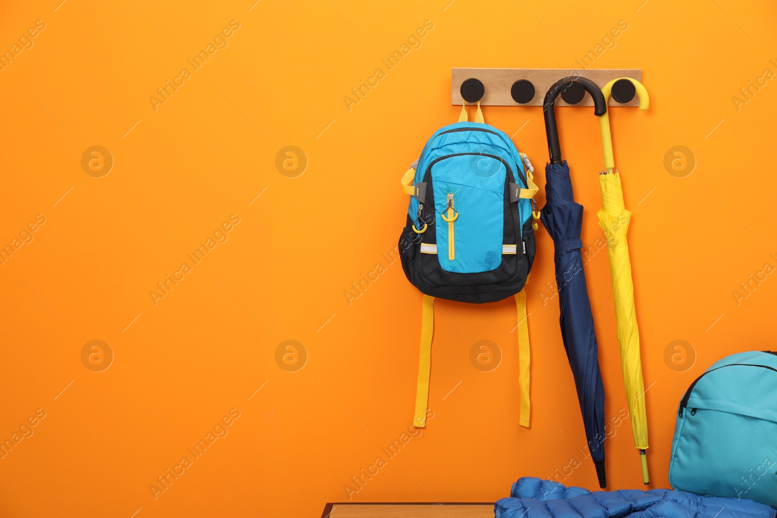 Photo of Colorful umbrellas, backpacks and blue jacket on bench near orange wall, space for text