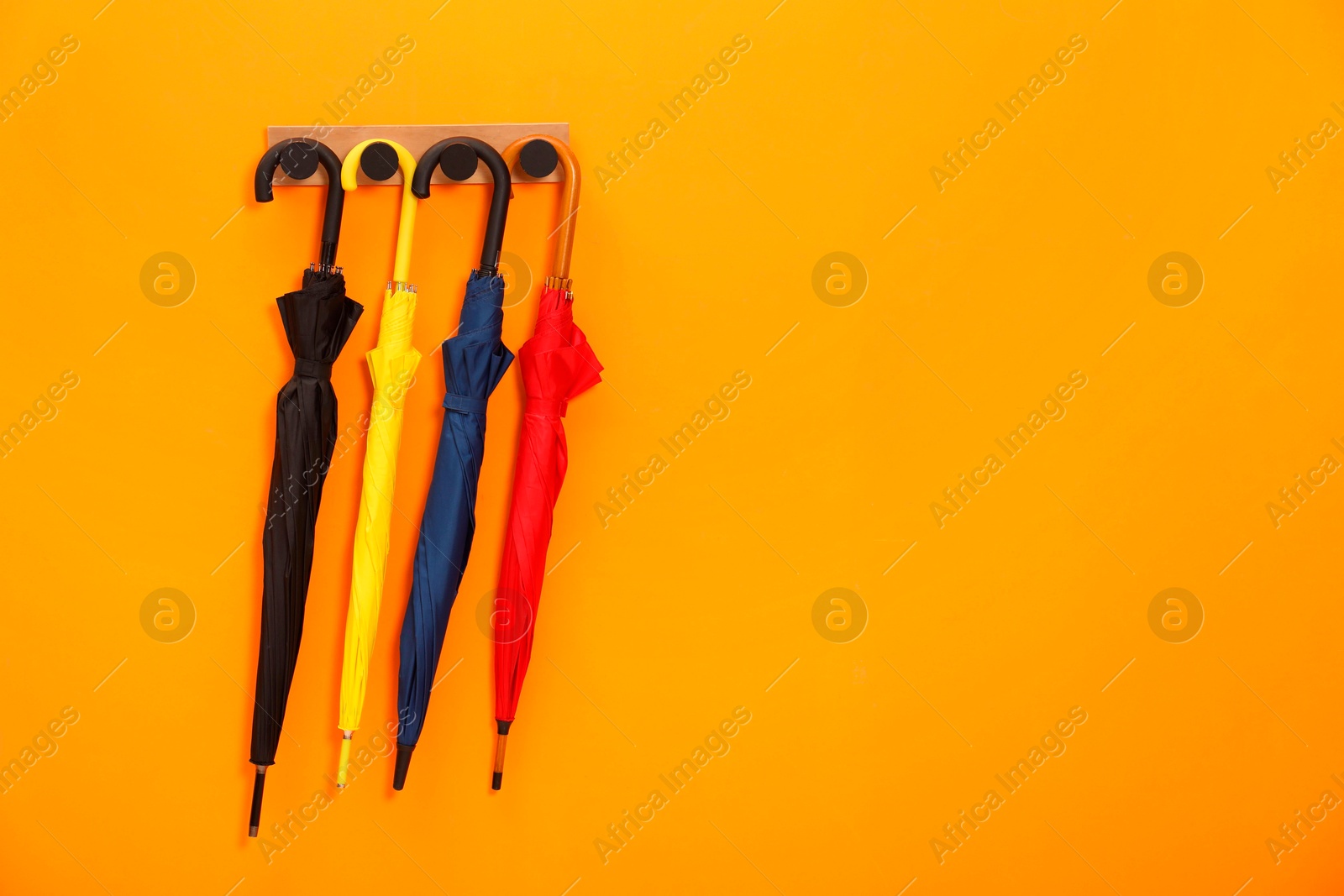 Photo of Colorful umbrellas on wooden rack in hallway, space for text